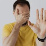 man met hand voor ogen en hand omhoog, dichtklappen, emotioneel bevriezen