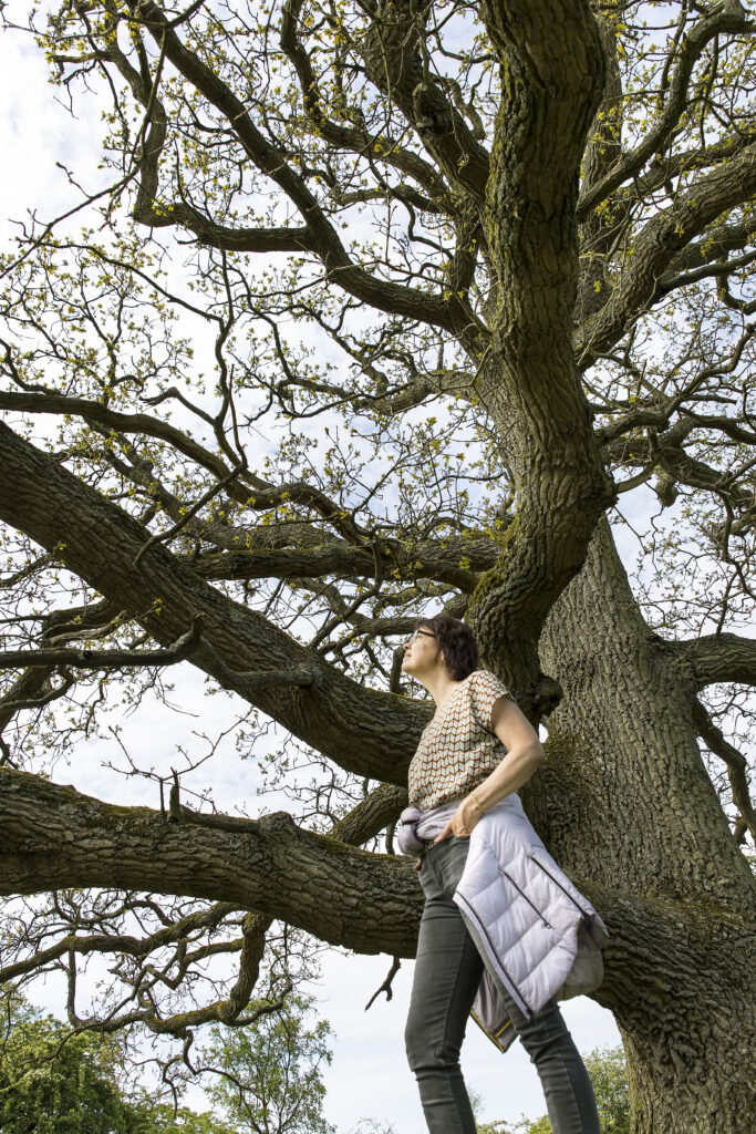 vrouw in overlevingsstand, rustend tegen de stam van een boom, omhoog kijkend